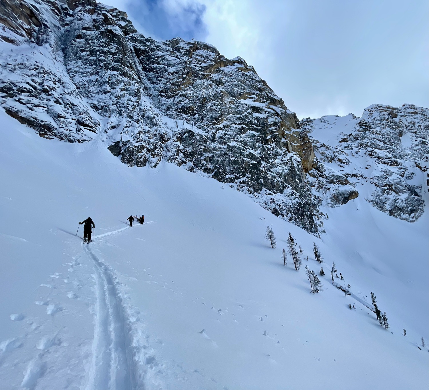 A group of backcountry skiers navigating through fresh powder snow in a scenic mountain setting.